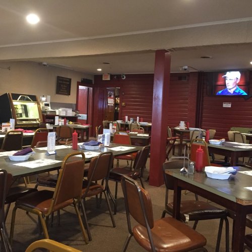 A cozy restaurant interior with empty tables, ketchup bottles, and a TV showing a program on the wall.