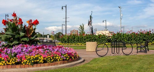 A vibrant flower garden with colorful blooms, benches, and a bicycle sculpture in a sunny park setting.