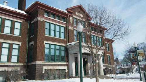 Historic brick building with green windows, snow-covered ground, and trees, under a clear blue sky.