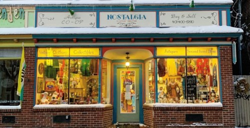 A colorful vintage shop window displaying antiques, clothing, and collectibles, with a sign reading "Nostalgia."