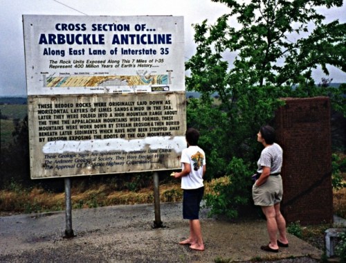 Two people stand in front of a large informational sign about the Arbuckle Anticline along Interstate 35.