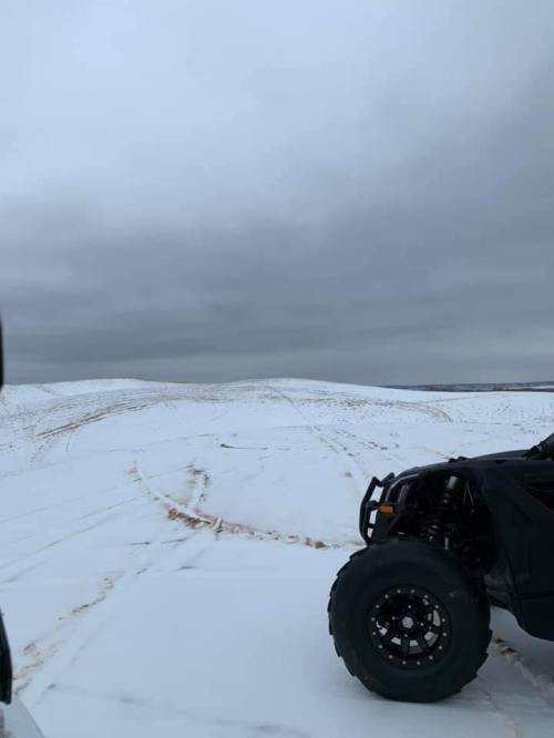 A rugged off-road vehicle parked on a snowy landscape under a cloudy sky, with distant hills visible.