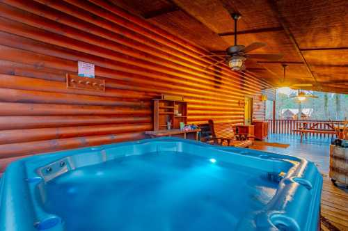 A cozy log cabin porch featuring a blue hot tub, wooden furniture, and warm lighting.