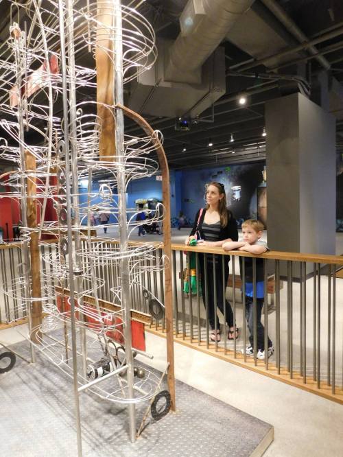 A woman and a child observe a large, intricate wire sculpture in a museum or play area.