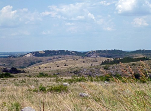 A scenic view of rolling hills and grassy plains under a partly cloudy sky.
