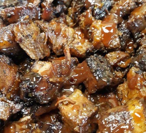 Close-up of tender, caramelized pieces of meat coated in a rich, glossy barbecue sauce.
