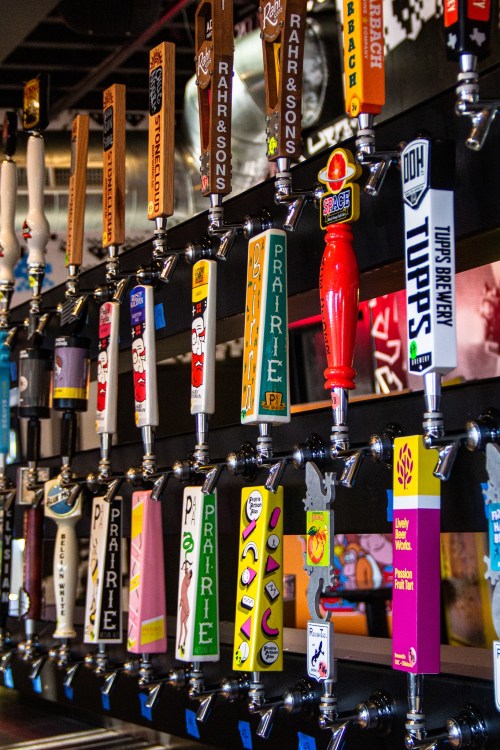 A row of colorful beer taps featuring various brewery logos and designs in a bar setting.