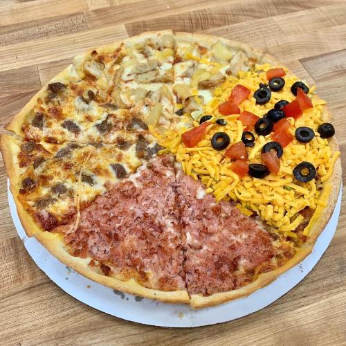 A pizza divided into four sections: chicken and pineapple, meat lovers, ham, and a mix of cheese, tomatoes, and olives.