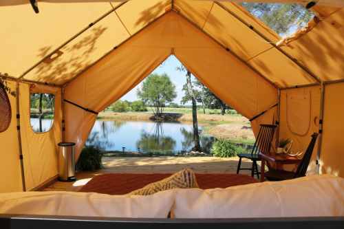 Cozy tent interior with a view of a serene pond and greenery outside.