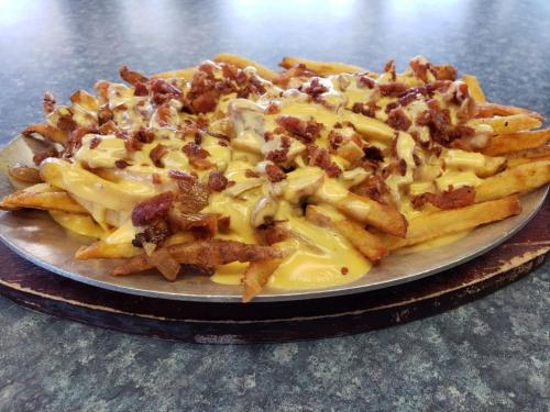 A plate of loaded fries topped with melted cheese, bacon bits, and sautéed onions on a blue countertop.
