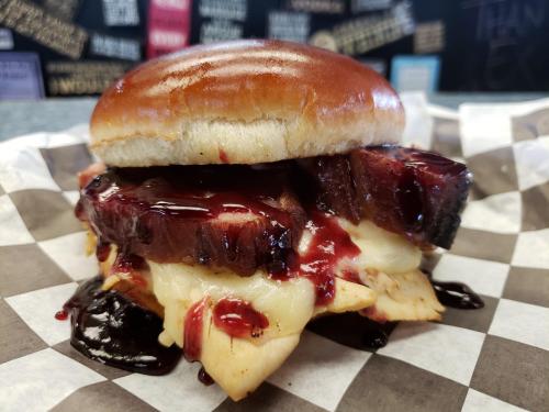 A close-up of a delicious sandwich with layers of meat, melted cheese, and a rich sauce, served on a toasted bun.