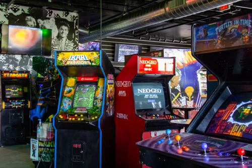 A vibrant arcade filled with classic game machines, including Ikari Warriors and Turtles in Time, under colorful decor.