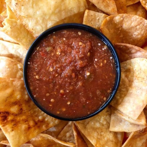 A bowl of salsa surrounded by crispy tortilla chips.