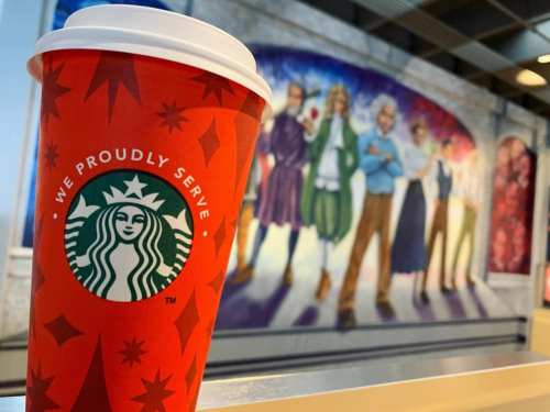 A festive Starbucks cup in front of a colorful mural featuring people in various outfits.