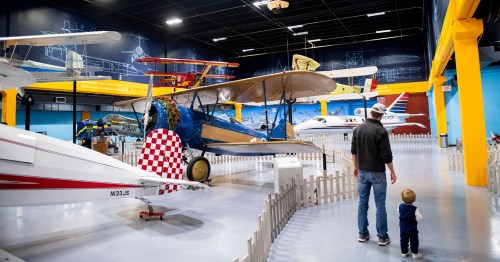 A man and a child explore an aviation museum filled with various aircraft and colorful displays.