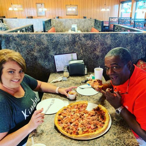 A man and woman enjoy a large pizza at a restaurant, smiling and sharing a meal together.