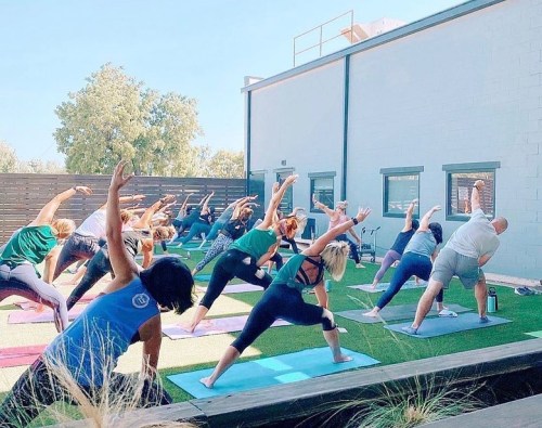 A group of people practicing yoga outdoors, stretching in various poses on mats under a clear blue sky.