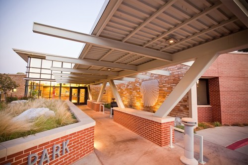 Modern building entrance with a stone facade, large overhang, and landscaped pathway leading to the doors.