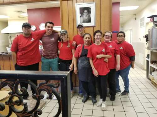 A group of eight people in red shirts poses together in a restaurant, smiling in a warm, welcoming environment.