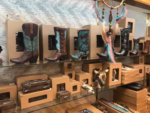 A display of colorful cowboy boots on shelves, with decorative items and boxes in a boutique setting.