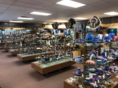 A spacious gallery filled with various pottery and decorative items displayed on glass shelves and wooden tables.