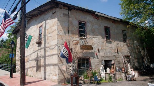 Historic stone building with flags, sculptures, and a sign, set against a clear blue sky.