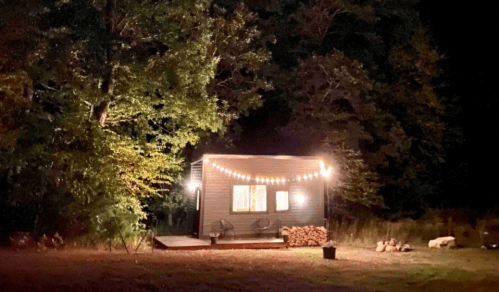 A cozy cabin illuminated by string lights, surrounded by trees at night.