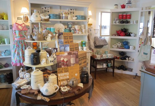 A cozy shop display featuring various teapots, mugs, and kitchenware on shelves and tables.