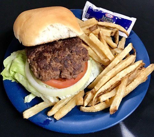 A plate with a hamburger topped with lettuce, tomato, and a side of fries, accompanied by a packet of ketchup.