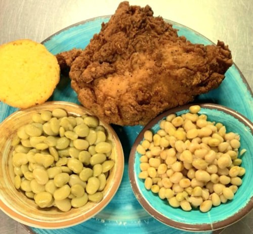 A plate with fried chicken, cornbread, and two bowls of green and yellow beans.