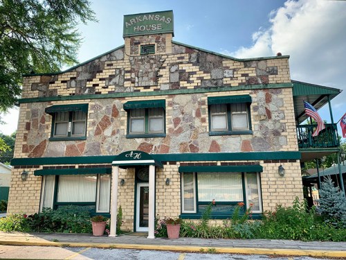 Historic building with stone and brick facade, featuring "Arkansas House" sign and flower pots at the entrance.