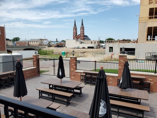 View of a patio with tables and umbrellas, overlooking a construction site and a church with twin spires in the background.