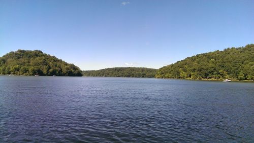 A serene lake surrounded by lush green hills under a clear blue sky.