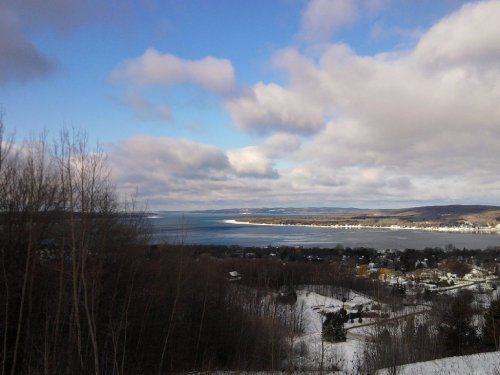 A scenic winter landscape featuring a lake, snow-covered hills, and a cloudy blue sky.