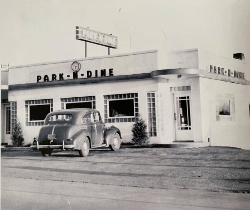 Black and white photo of a vintage car parked outside a diner named "Park-N-Dine."