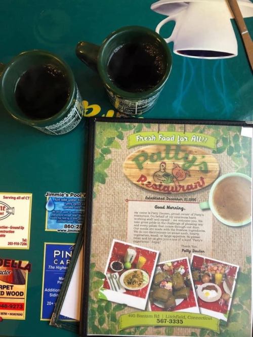 Two coffee mugs sit beside a menu for Patty's Restaurant on a green table. The menu highlights fresh food options.