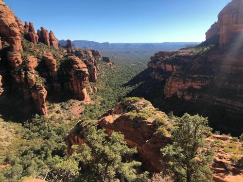 A panoramic view of red rock formations and lush green valleys under a clear blue sky.