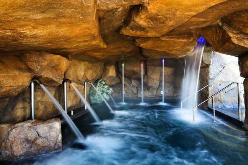 A serene spa area with a rocky cave, featuring flowing water and colorful lights illuminating the space.
