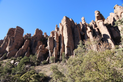Tall, jagged rock formations rise against a clear blue sky, surrounded by sparse vegetation.