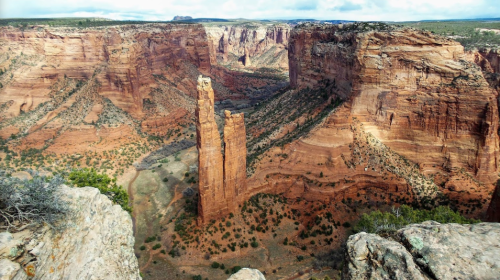 A stunning view of a canyon with towering rock formations and lush greenery amidst red and orange cliffs.