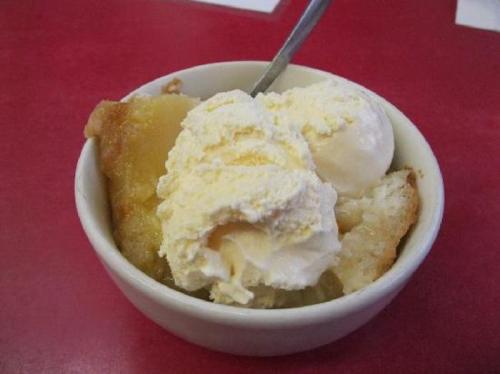A bowl of warm dessert topped with two scoops of vanilla ice cream on a red table.