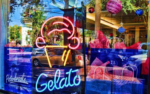 Neon sign of an ice cream cone with the word "Gelato" in a colorful shop window decorated for the holidays.