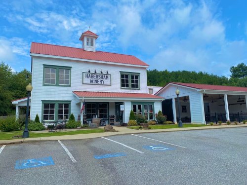 Exterior of Habersham Winery, featuring a white building with a red roof, surrounded by greenery and parking spaces.