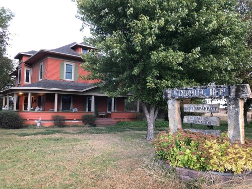 A charming two-story orange bed and breakfast with a sign, surrounded by trees and grassy areas.