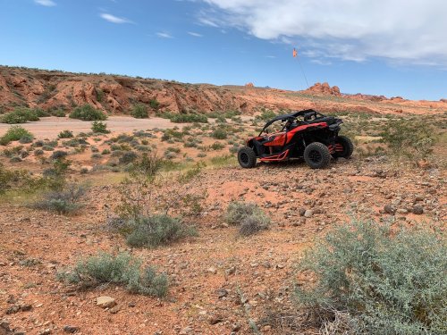 An off-road vehicle parked on rocky terrain with red rock formations and sparse vegetation in the background.