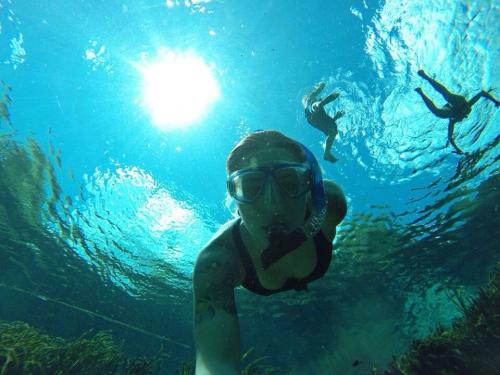 A person snorkeling underwater with two others in the background, surrounded by clear blue water and sunlight.