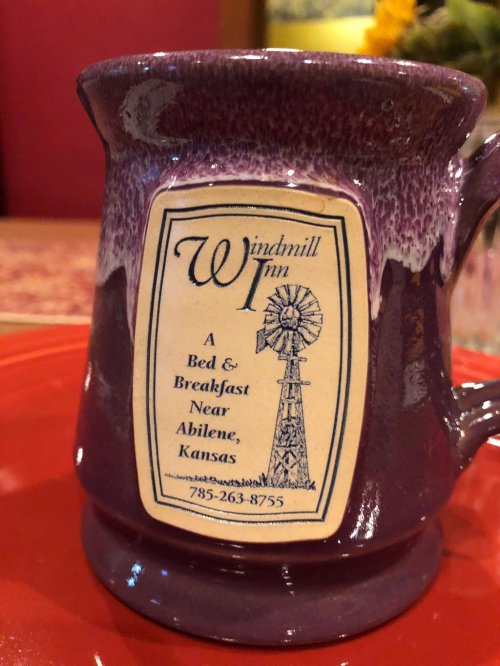 A purple mug featuring a logo for Windmill Inn, a bed and breakfast near Abilene, Kansas, with a windmill design.