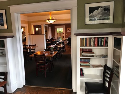 A cozy restaurant interior with wooden tables, bookshelves, and warm lighting, creating an inviting atmosphere.
