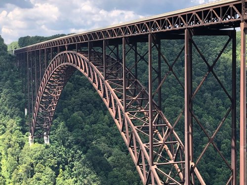 A large, arched metal bridge spans a lush green valley under a partly cloudy sky.
