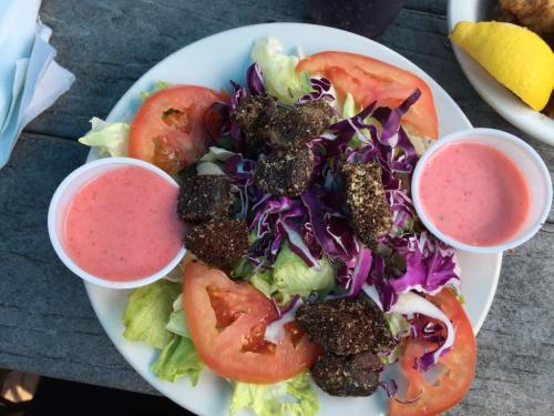 A colorful salad with lettuce, tomatoes, purple cabbage, and fried bites, served with two cups of pink dressing.